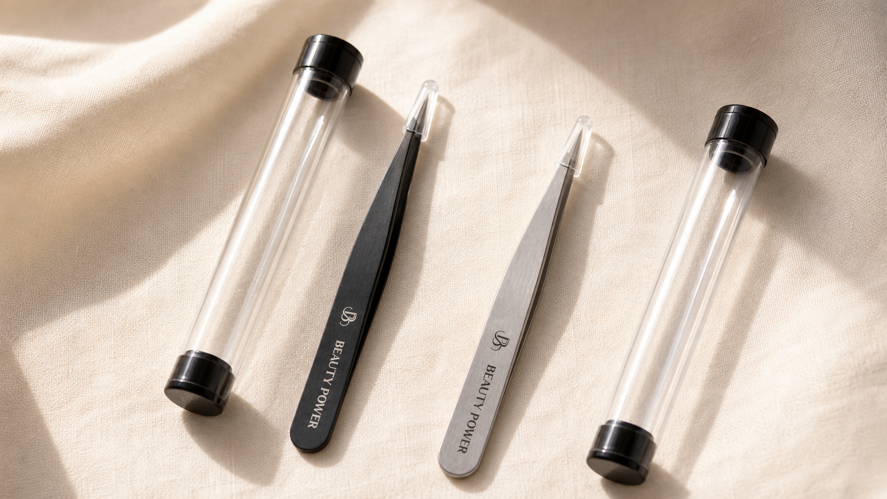 Beauty Power Ultra Precision Point Eyebrow Tweezers Gray and Black flat lay on cream linen
