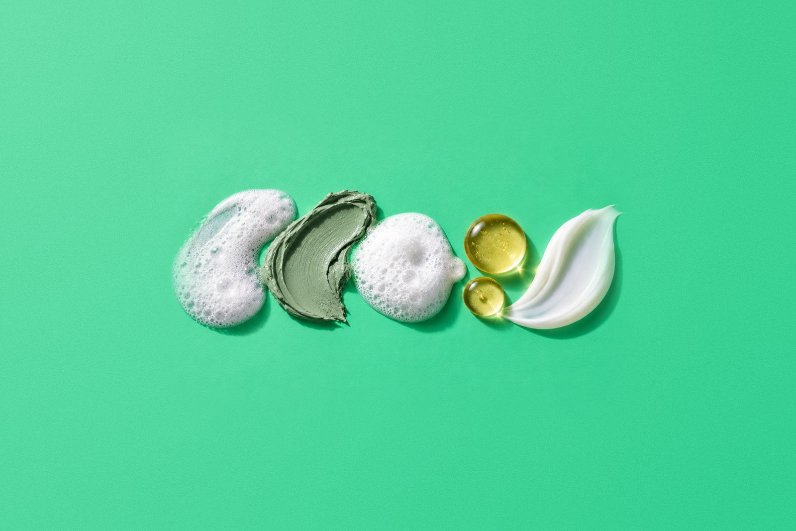 Skin detox home care routine textures in order: foam cleanser, gray Illite clay mask, oxygen bubble foam, golden EGF ampoule drops and peptide cream on mint green